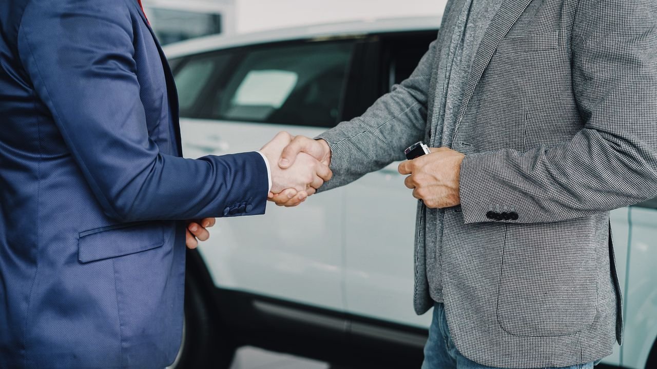 Two businessmen shaking hands in a car dealership, sealing a deal.