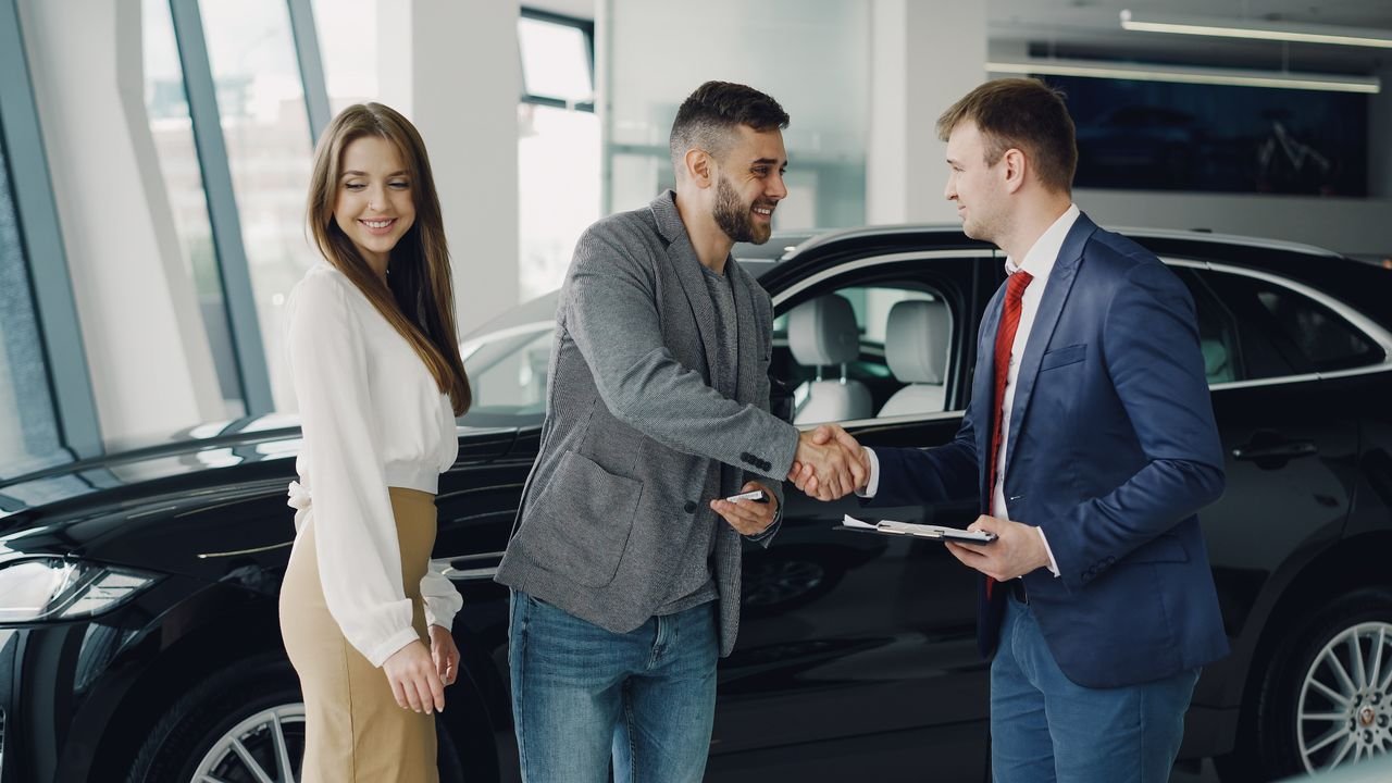 Buyers and sales representative shake hands at a car dealership for a successful car purchase.